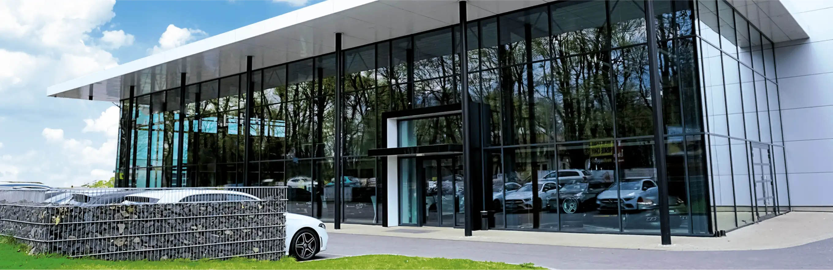 Un edificio commerciale con auto parcheggiate e un'area verde antistante - nelle vicinanze ci sono vari negozi e servizi.